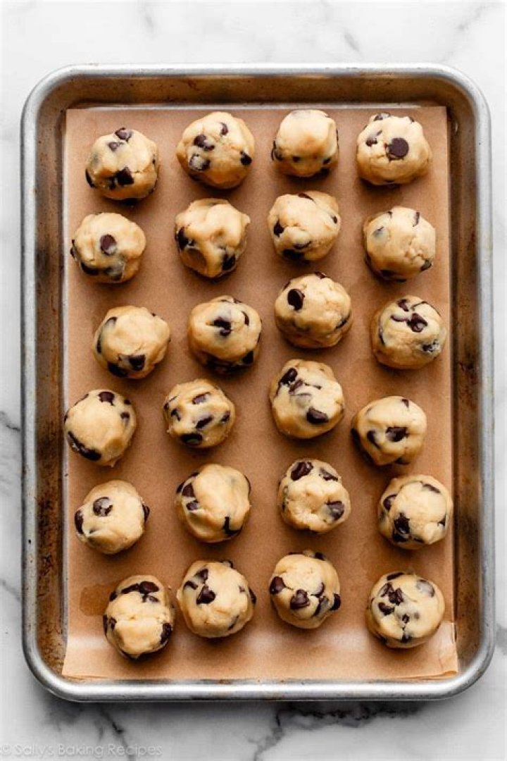 Large cookie dough balls on a parchment lined baking sheet.